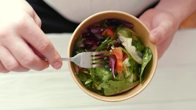 Closeup of man eating a fresh healthy salad from a zero waste container to go. Food delivery, healthy food concept.
