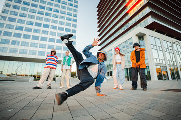 Energetic young people showcasing incredible breakdancing skills in urban environment with friends...