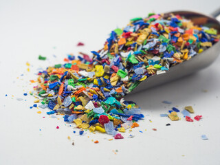 Various colors of plastic waste that has been ground in a stainless shovel on a white background