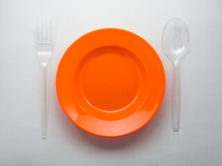 Empty orange plastic plate with clear spoon and fork isolated on white background