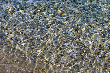 Shiny sea surface above a pebble beach with light reflections