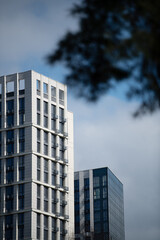 Fototapeta premium Two towering modern buildings feature striking designs, standing tall under a cloudy sky in an urban landscape. The structures display a mix of glass and concrete elements
