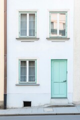 Two windows and a mint-green door create a charming facade of a residential building on a quiet street in a European town during the day