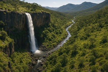 Majestic Waterfall Cascade Flowing into Serene River Valley Surrounded by Lush Greenery and Mountains