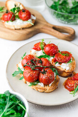 Bruschetta with cottage cheese, arugula and roasted cherry tomatoes. Food photo.