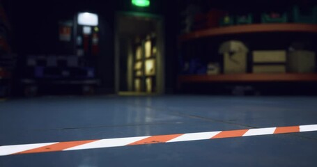 A wide view of a dimly lit warehouse interior captures caution tape marking boundaries on the polished floor. The environment suggests a space used for storage and assembly.