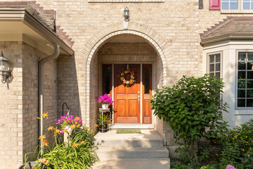 A front door detail on a brick home with an arched entryway, wooden front door, and beautiful landscaping.