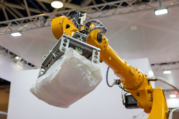 An industrial robotic arm with a pneumatic gripper lifts a heavy white bag in a factory setting....