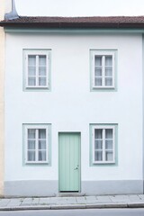 Obraz premium The design of a charming light blue house, adorned with vibrant green accents, stands out beautifully against the backdrop of urban surroundings during the bright daylight hours
