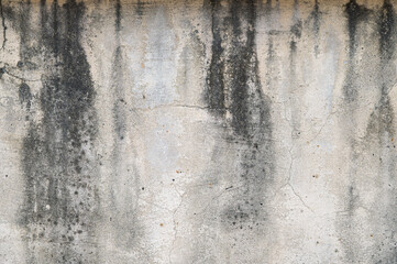 A weathered concrete wall with dark stains and peeling paint, showcasing an aged texture. The rough surface and muted colors evoke an urban, industrial, and rustic feel.