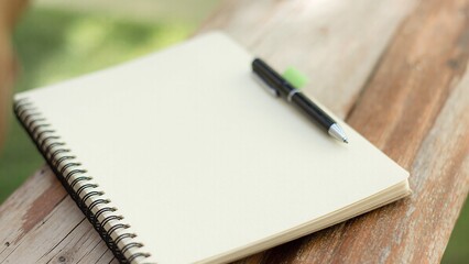 Open notebook rests outdoors near a pen on a wooden surface for note-taking or planning