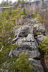 Male hiker with a backpack climbs a metal stairway carved into towering sandstone rocks in Saxon Switzerland, capturing an adventurous outdoor ascent.