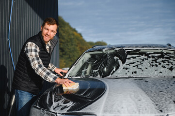 A man washes a car with a sponge at a self-service car wash