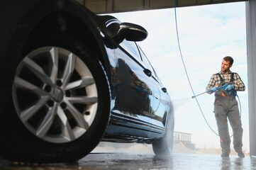 Man worker in uniform washing standing front car service station. Car wash cleaning station
