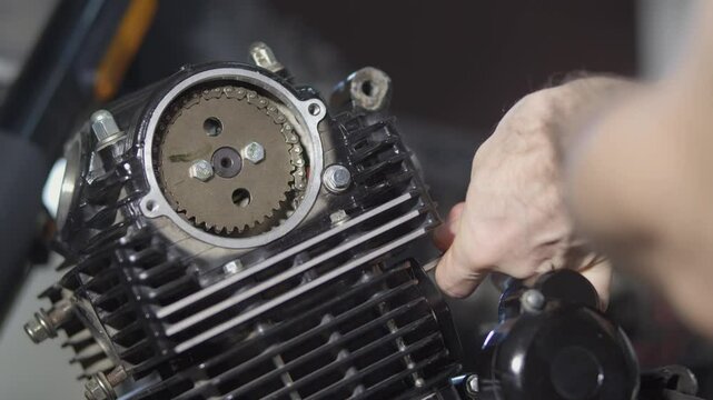 A mechanic is repairing a motorcycle engine, he is tightening the cylinder head chain tensioner bolts with an hex key