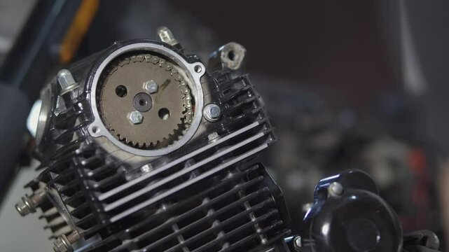 A mechanic is repairing a motorcycle engine, he is cranking the engine and checking the tension of the cylinder head chain