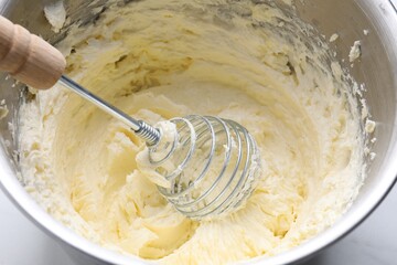 Whisking whipped cream in bowl on white table, closeup
