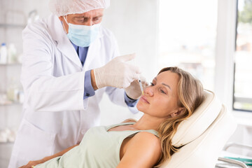 Obraz premium Middle-aged female patient lying on clinical chair undergoing face care procedure by injection method