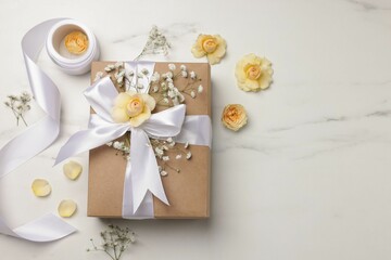 Florist. Box, flowers and ribbon on white marble table, flat lay. Space for text