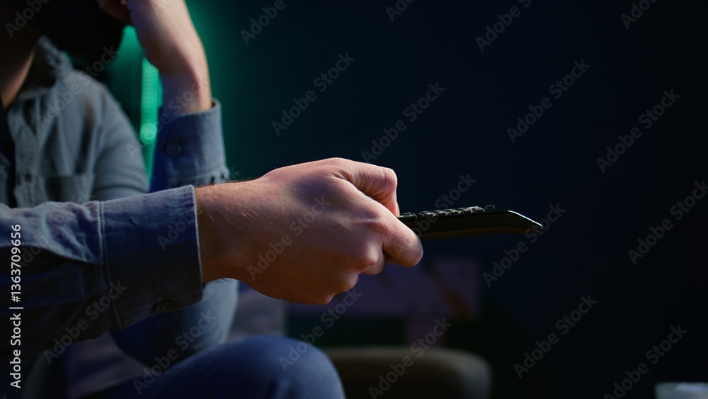 Aufkleber close up of man on couch using remote control to browse though movies available on streaming service