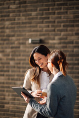 Two businesswomen having a casual meeting outdoors, laughing and using tablet