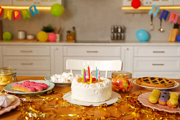 Tasty cake with burning candles and different treats on table indoors. Birthday surprise party