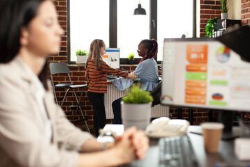 Selective focus of caucasian little girl playful disturbing african american lady employee in modern office. Black woman speaking with female child before working on computer in startup company.