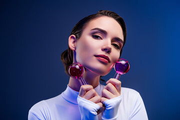 Stylish young woman with beauty tools posing in neon blue light wearing modern white bodysuit