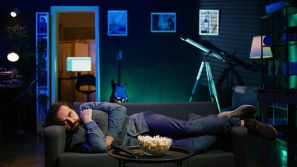 Man laying down hugging pillow watching TV, heartbroken by upsetting movie plot. Sad viewer lounged...