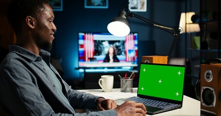 Teleworker at home editing documents next to mockup on his laptop, submitting reports and files before deadline. Black freelancer managing digital paperwork within the work platform. Camera A.