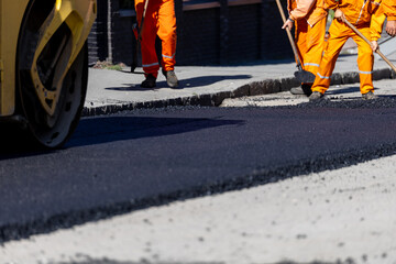 Construction workers laying asphalt on a city street in broad daylight
