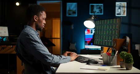 Financial advisor examines cryptocurrency trade market from his loft workstation, looks at online global exchange statistics on desktop. Guy studying stock analysis to secure capital funds. Camera A.