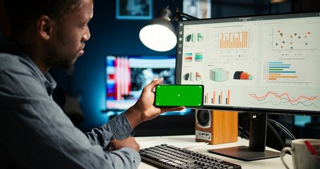 Young person does remote work using data finances with a green screen, examining statistics at his...
