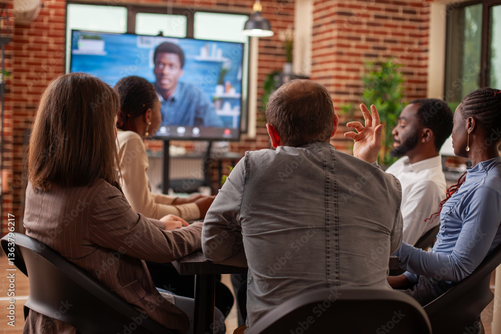 Poster caucasian man and colleagues attentively listen to virtual client presentation displayed on monitor 