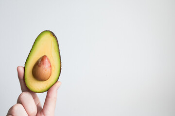 Hand holding halved avocado against minimalist white background