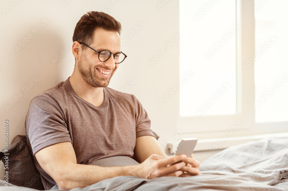 Poster Smiling Man Using Smartphone Mobile App Sitting In Bed At Home On Weekend Morning. Free Space For Text
