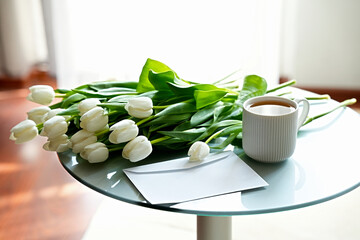 Bouquet of white tulips, coffee cup and white clean envelope on round glass table with white background