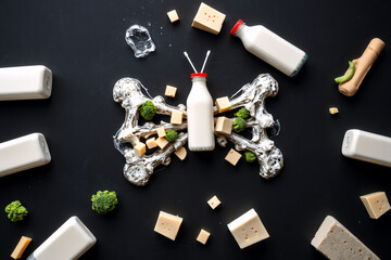 Healthy food flat lay featuring milk bottles, cheese cubes, and broccoli florets creatively arranged to resemble a butterfly on a dark surface.