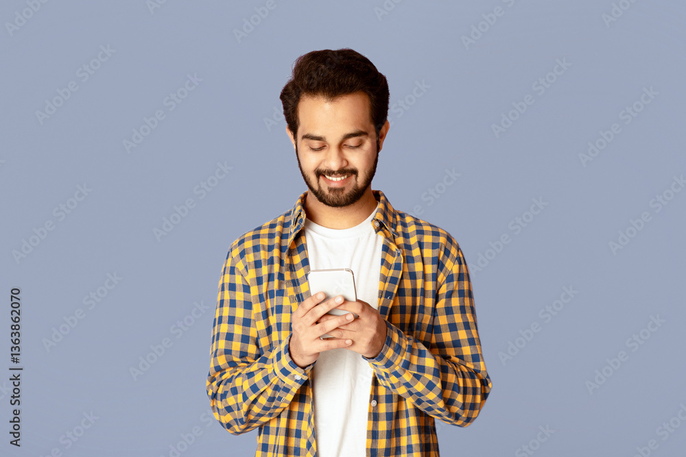 Poster positive indian man looking at mobile phone screen and smiling on violet background
