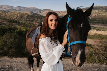 Close-up. A romantic girl hugs her horse against the backdrop of a mountain-plain landscape. The concept of riding. Artistic photography. Ready-made cover for books and magazines.