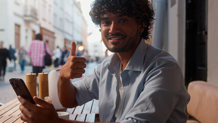 Arabian latino man guy visitor cafe buyer happy customer businessman drink coffee outdoor using mobile phone online shopping outside Indian male tourist showing thumb up approve travel app smartphone