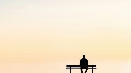 Obraz premium A solitary figure sits on a bench against a serene, pastel sky, evoking feelings of reflection and tranquility.