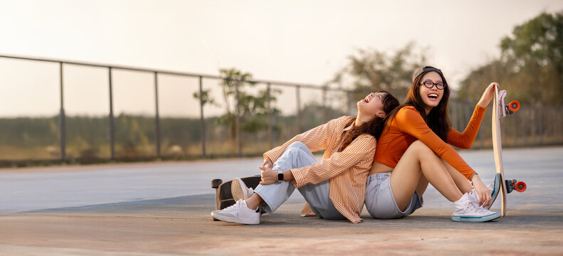 Happy young Asian girls with classmate students having fun skateboarding together in skate park, Friend happiness moment, Widescreen with copy space.
