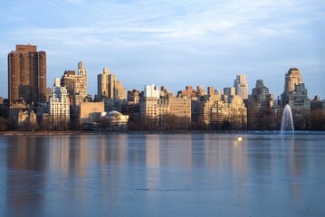 NYC 5th Ave skyline from across a pond, the Jacqueline Kennedy Onassis Reservior, taken near dusk. Taken while walking in Central Park, New York City on a clear winter day.