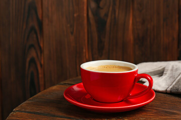 Red cup with coffee on wooden table, space for text