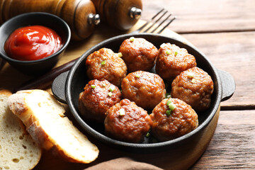 Tasty meatballs with green onion in baking dish served on wooden table