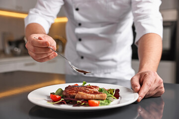 Professional chef adding sauce to delicious dish at table indoors, closeup