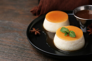 Tasty puddings with caramel sauce served on wooden table, closeup. Space for text