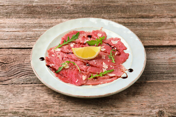 Delicious beef carpaccio with arugula, cheese, balsamic vinegar and lemon on wooden table