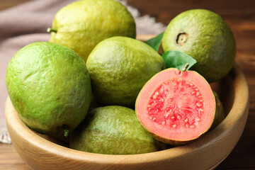 Fresh cut and whole guava fruits in bowl on table, closeup